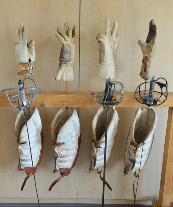 Schutzkleidung, Handschuhe und Schlagwaffen für das akademische Fechten, ordentlich an einer Holzwand aufgehängt